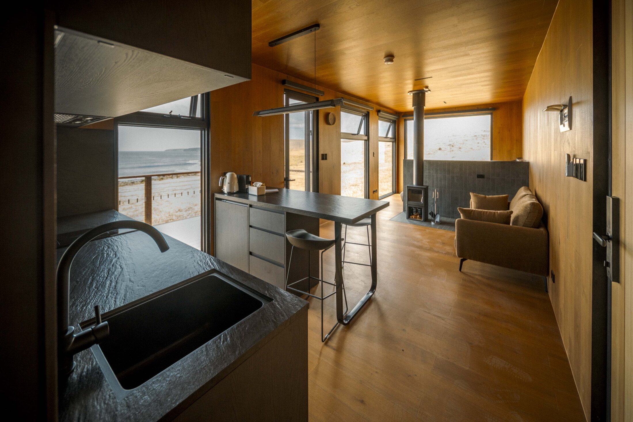Inside an AUTRA cabin — warm timber, a wood stove and an ocean view